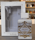 BADEE AL OUD HONOR & GLORY, perfume en frasco cuadrado plateado con detalles geométricos dorados y caja a juego.