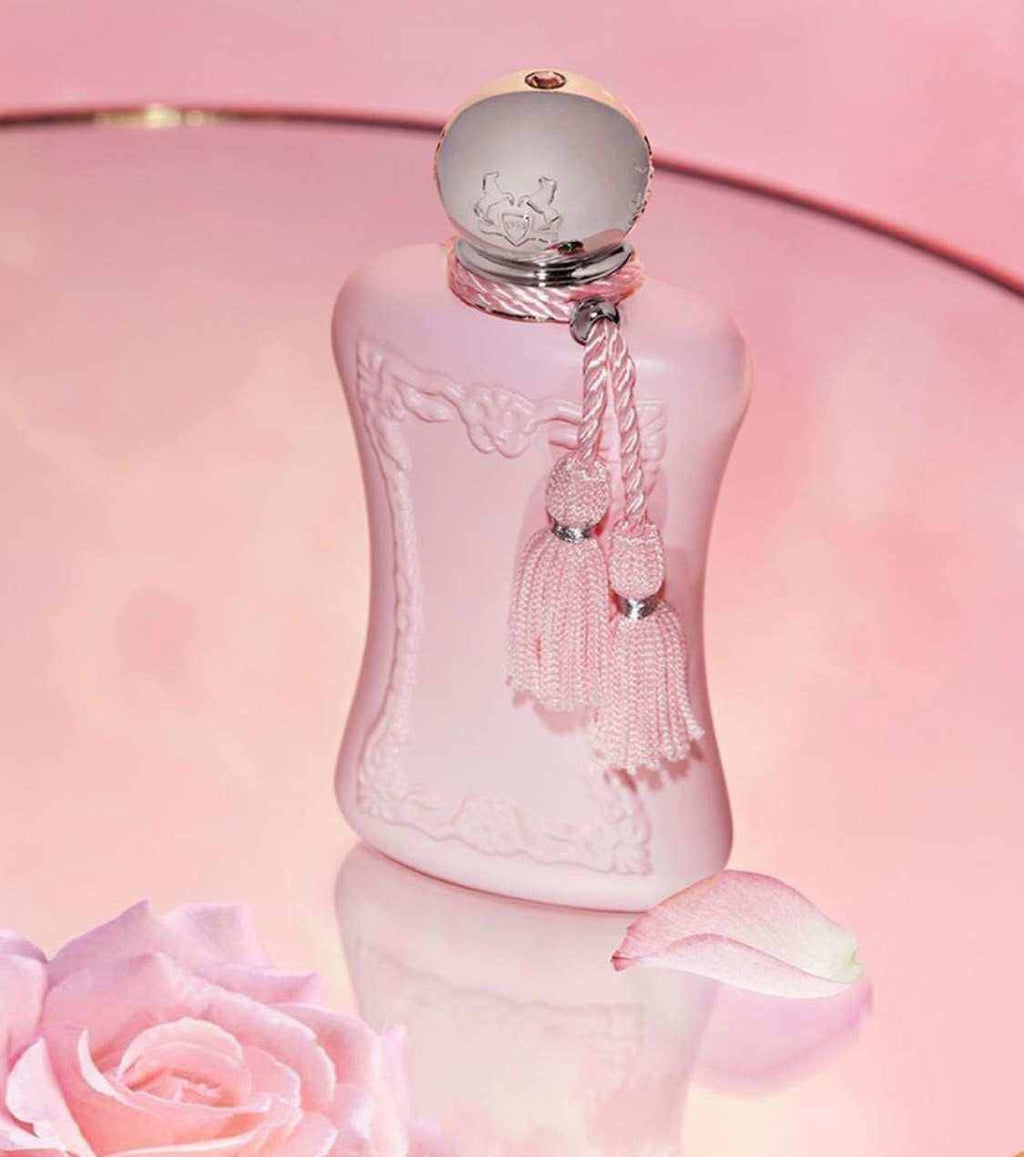 Delina Eau de Parfum en frasco rosa pálido con relieves florales, tapón plateado y borla decorativa