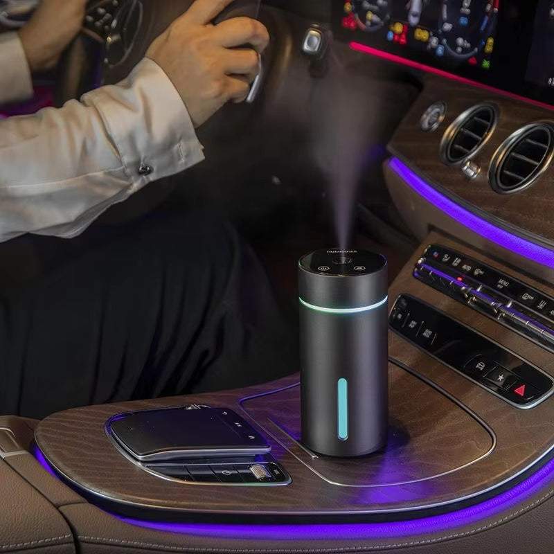 Humidificador portátil para coche cilíndrico negro y plateado, con bandas luminosas y vapor visible en el salpicadero.
